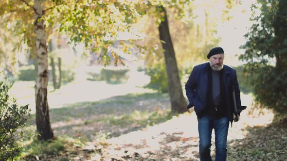 Old Painter Walks in a Sunny Park and Looks Around alt