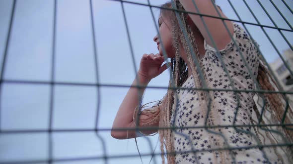 Young Girl with Dreadlocks Poses at the Fence