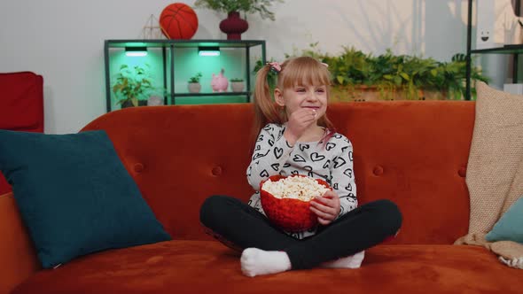 Funny Children Girl Watching Comedy Video Film on Tv Eating Popcorn on Comfortable Sofa at Home alt