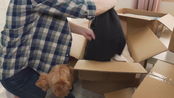 A Woman is Preparing to Move to a New House Putting Clothes in Cardboard Boxes