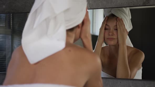 Caucasian woman looking in mirror after shower in hotel alt