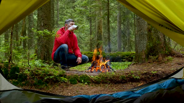 Bearded Man Tourist Near the Fire in a Beautiful Forest alt