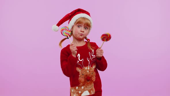 Joyful Girl in Christmas Sweater Hat Holding Candy Striped Lollipops Dancing Making Silly Faces alt