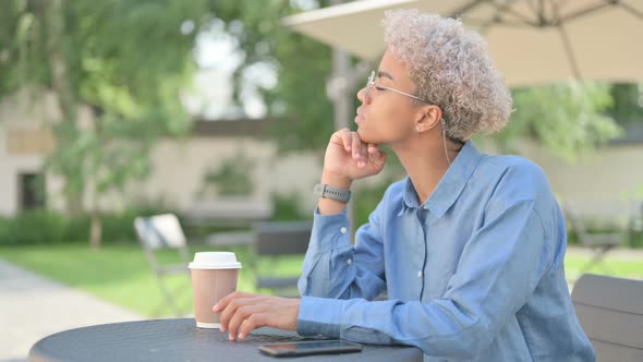 Young African Woman with Coffee Thinking in Outdoor Cafe alt