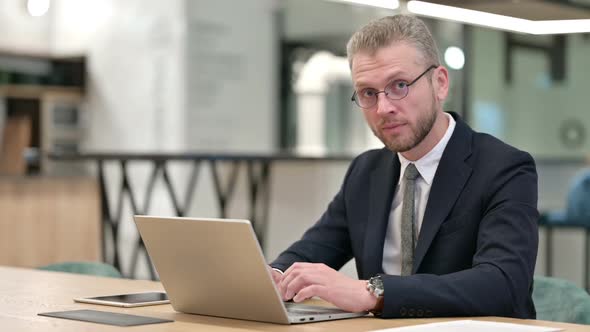 Young Businessman with Laptop Smiling at Camera in Office alt