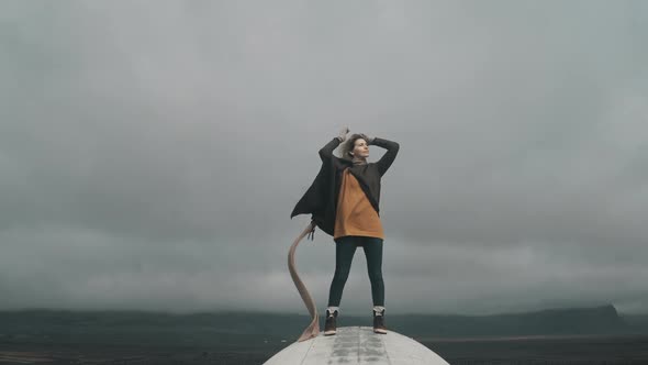 Freedom: Young Blonde Woman Standing on the Top of Crashed DC-3 Plane in Iceland and Raising Hands alt