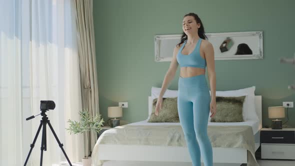 Fit brunette woman in blue sportswear making video for blog morning workout with exercises at home alt