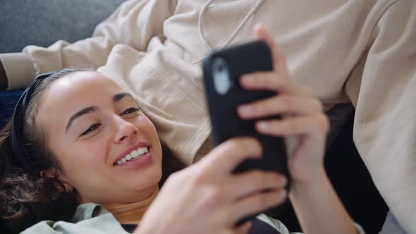 Close Up Of Woman Resting On Partners Lap At Home On Sofa Checking Social Media On Mobile Phone