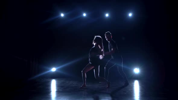Young Couple Dancing Contemp Against Black Background with Spotlights at Studio. alt