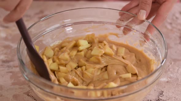 Mixing ingredients in a large glass mixing bowl to making apple cake.