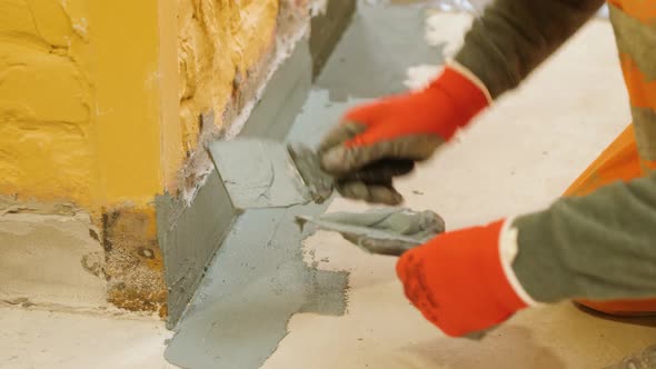 Hands Use a Spatula to Putty the Protrusion of the Wall with the Floor