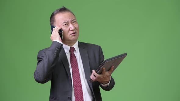 Mature Japanese Businessman Working with Digital Tablet and Phone alt