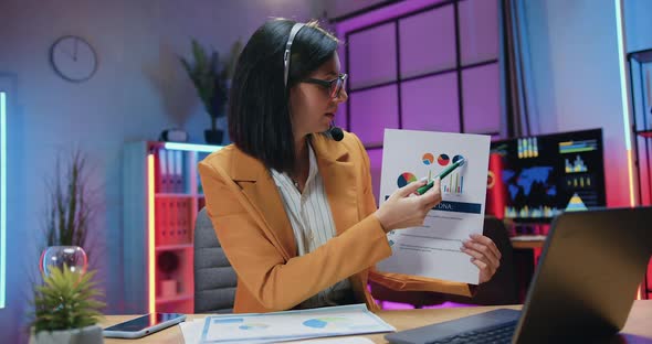 Brunette in Headset and Glasses Sitting in front of Laptop During Online Chat alt