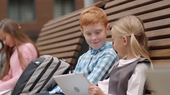 Caucasian Schoolgirl and Schoolboy Using Tablet Outdoors alt