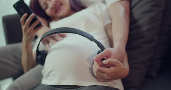 Happy Asian husband and pregnant wife spend time together turning on music for an unborn baby.