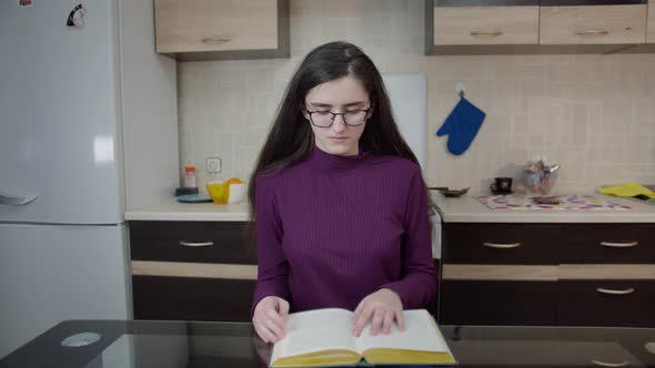 Brunette Girl Sitting in the Kitchen in the Evening and Studying School Material alt