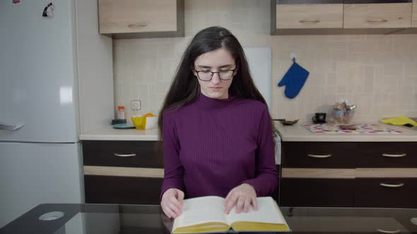 Brunette Girl Sitting in the Kitchen in the Evening and Studying School Material