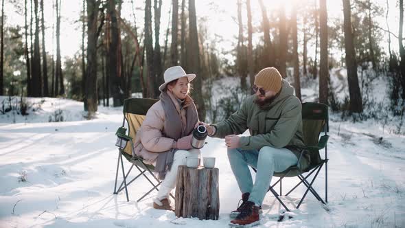 Romantic Couple Drink and Talk in the Woods in Winter Enjoying Camp Life