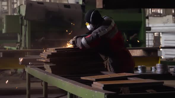 Heavy Industry Engineering Factory Interior with Industrial Worker Using Angle Grinder and Cutting a