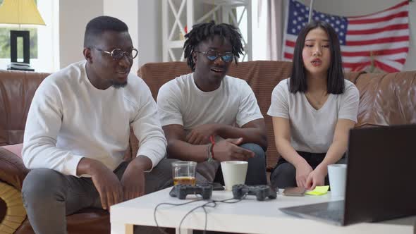 Absorbed Multiethnic Friends Watching Match on Laptop Making Disappointed Facial Expression Talking alt