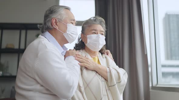 asian retired elderly couple wearing face masks watch the world through their home