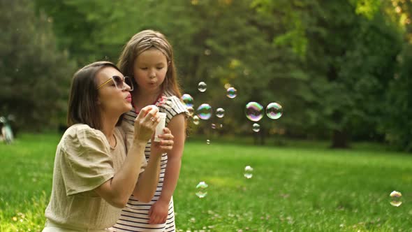 Young Woman and Her 6 Year Old Daughter are Blowing Rainbow Soap Bubbles