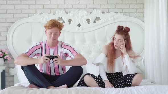 Irritated Woman Looking at Redhead Man Playing Video Games. Portrait of Young Caucasian Couple alt