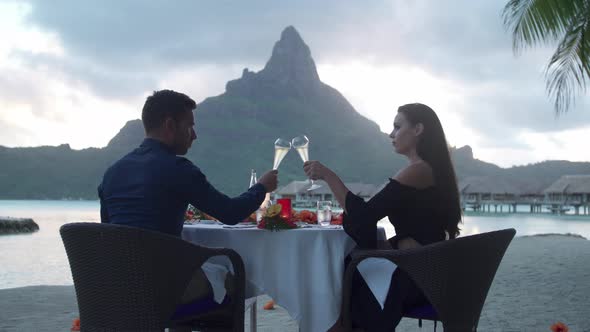Man and woman couple toasting with champagne on beach, tropical island resort sunset, Bora Bora alt