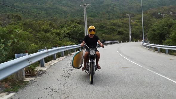 Person Driving Motor Scooter With Surfboard On Side In Vietnam. Tracking Shot alt