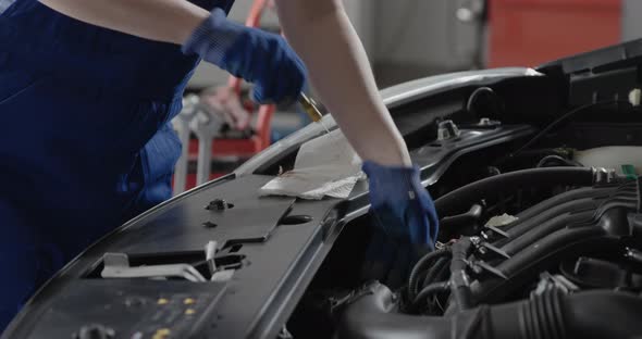 Professional female mechanic checking a car's engine oil using a dipstick