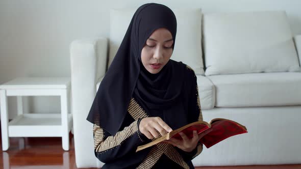 Young Muslim female wearing Islamic clothes reading the Quran