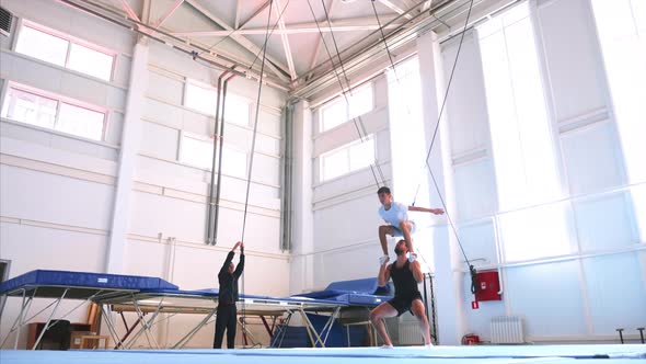 An Young Athlete is Doing an Air Back Flip on Safety Slings in the Gym alt