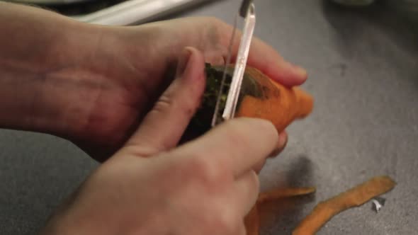 A view of the hands of a woman who peels carrots in the kitchen. film grain