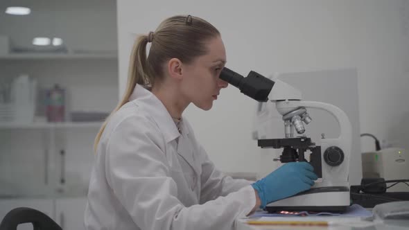 Female Medic in Uniform Working with Microscope Making Analysis at Laboratory Office alt