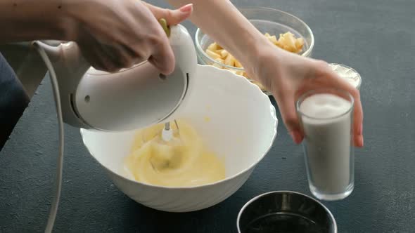 Woman's Hands with a Mixer Whisk Eggs in a Bowl and Add Sugar. Cooking Apple Pie.