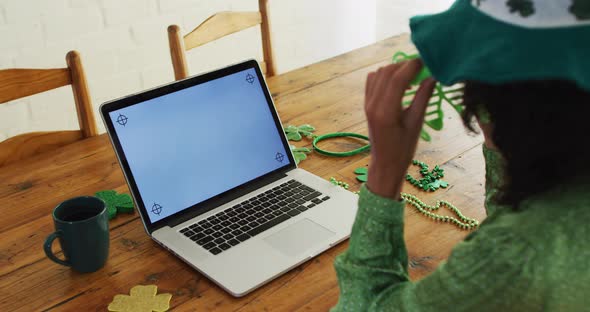 Mixed race woman in green glasses and costume having a video call on laptop at home alt