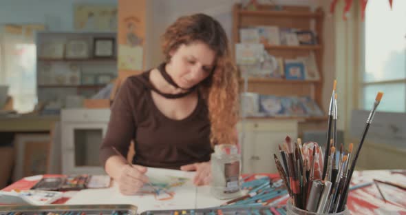 Female artist painting in her studio with water colors and pencils alt
