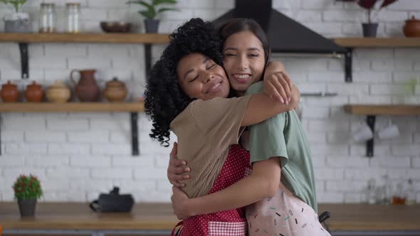 Live Camera Approaches to Happy Smiling African American and Asian Women Hugging in Kitchen alt