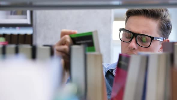 College Library. Male Student Searching For Book On Bookshelves alt