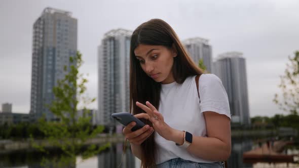 A Young Girl Browsing the News Feed is Very Upset Sitting on the Street in a Modern City the Girl is