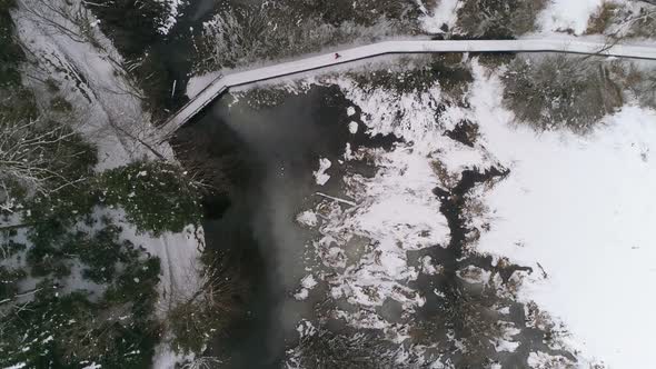 Aerial view of person running over wooden path next to frozen lake with forest covered in snow alt