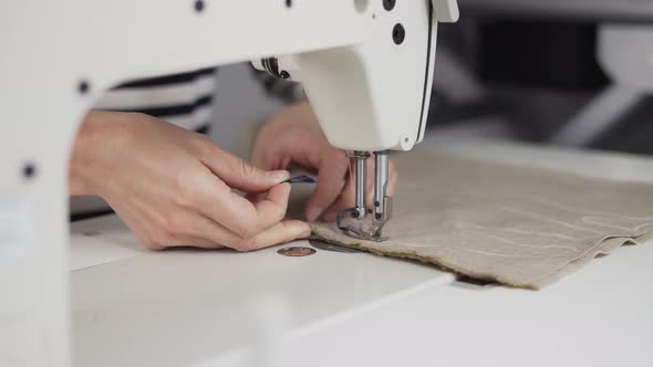 Closeup of a Young Woman's Hands Sewing Beige Fabric with a Sewing Machine alt