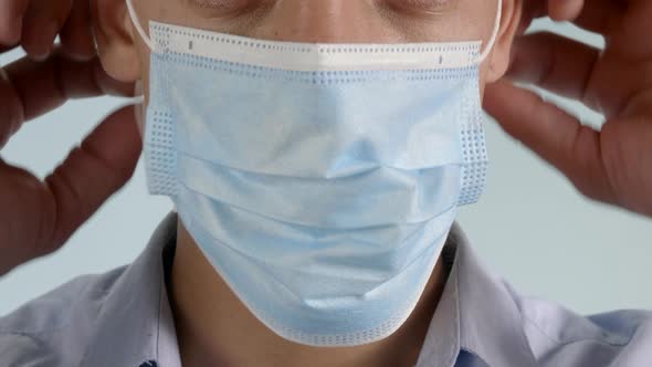 Smart young male fixing surgical face covering corona virus mask and adjusting close up alt