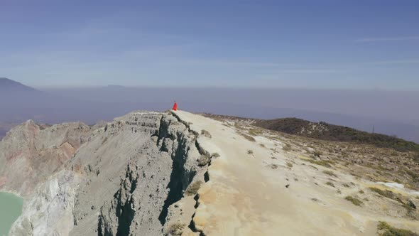 Drone View of Young Girl in Red Dress on Edge of Cliff alt
