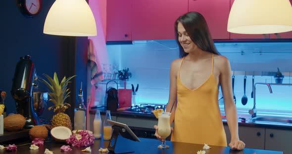 Young woman drinking alcoholic cocktail and speaking online using tablet alt