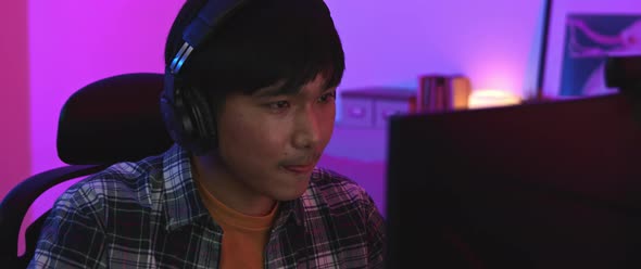 Asian man gamer wearing headphones focusing on playing e-sports