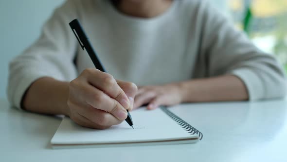 Closeup of a woman writing on a blank notebook on the table