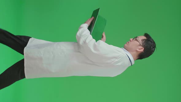 Asian Doctor With Stethoscope Reading Document While Walking On Green Screen alt