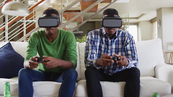 African american teenage twin brothers on couch using vr headsets and playing computer game smiling alt
