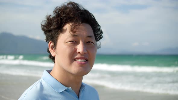 Portrait of a Middleaged Asian Man in a Blue Shirt Standing on the Beach By the Sea Against the alt